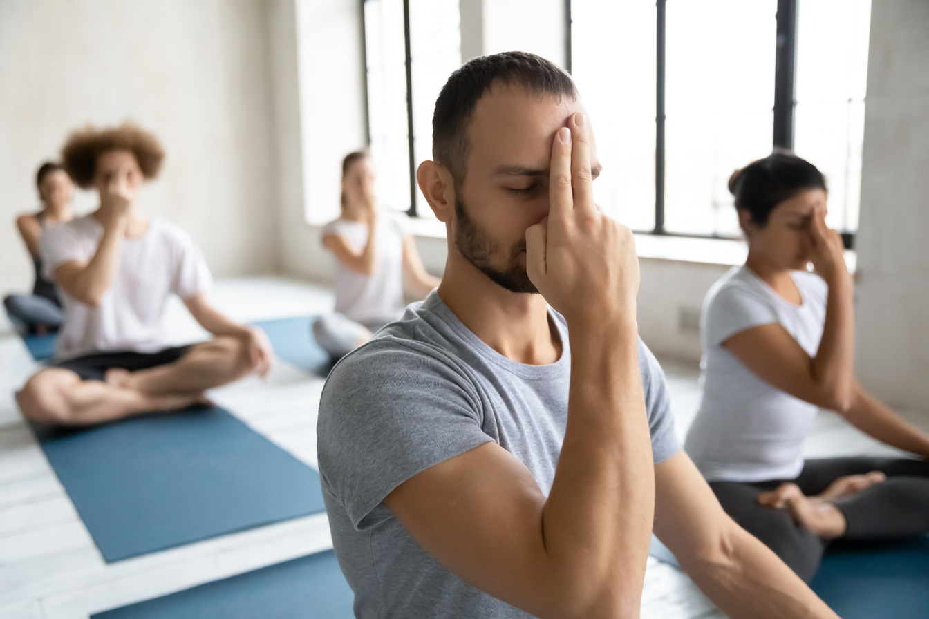 Young mindful male trainer showing Alternate Nostril Breathing to students.